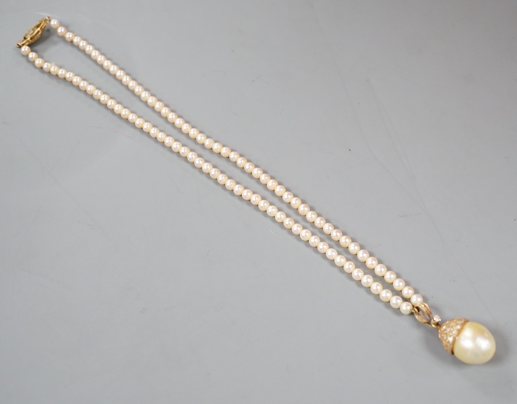A modern cultured pearl and diamond cluster set drop 'acorn' pendant, overall 23mm on a cultured pearl necklace with 18k clasp, necklace 36cm.